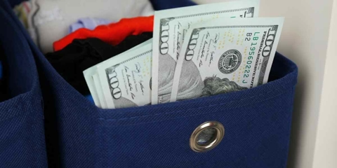 Hundred dollar bills that seem to be stuffed in a container filled with socks and other laundry items