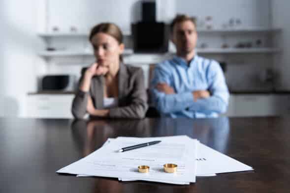 couple sitting next to each other behind divorce papers and wedding rings